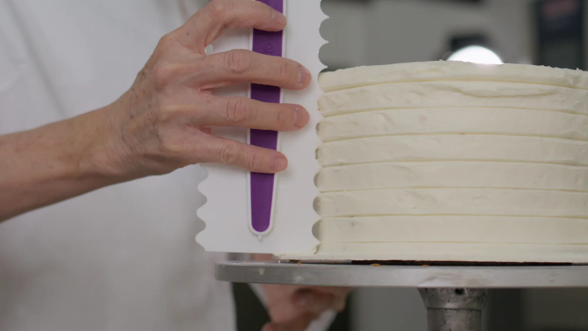 A pastry chef smoothing white icing on a layer cake